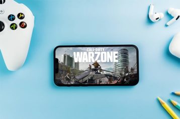 An image featuring a controller and mobile phone that has Call of Duty Warzone opened
