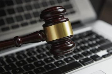 An image featuring a gavel with a laptop in the background concept