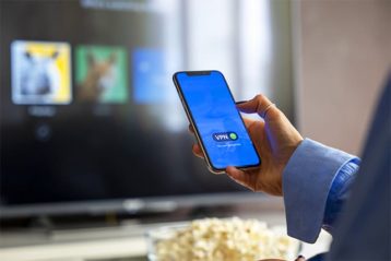 An image featuring a person using their mobile phone with VPN connection and watching TV concept