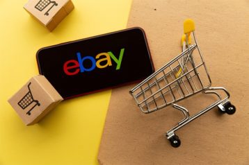 An image featuring a mobile phone that has eBay opened and multiple shopping carts representing eBay online shopping concept