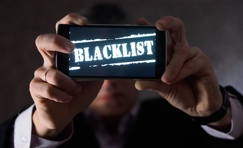 a man holding up a smartphone with Blacklist on the screen