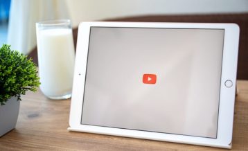 a white tablet running the YouTube application next to a glass of milk