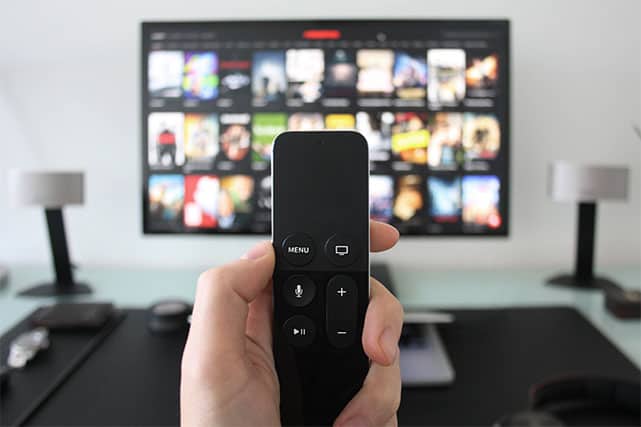 An image featuring a person holding out his TV remote and watching streaming TV
