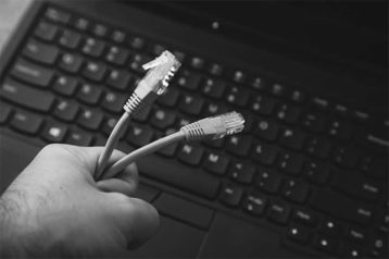 An image featuring a person holding out his ISP cable with a laptop in the background representing ISP blocking torrenters