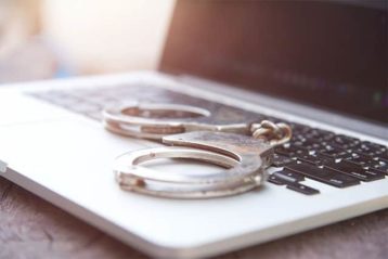 An image featuring a laptop with handcuffs on top of it representing torrenting jail