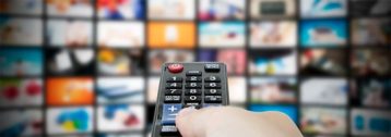 An image featuring a person holding out his TV remote and accessing multiple channels on TV