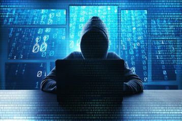 An image featuring a person wearing a dark hoodie and using his laptop representing a hacker with a hacker-ish background concept