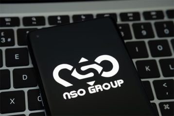 An image featuring the logo of NSO Group on a phone on top of a laptop