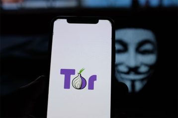 An image featuring a anonymous person wearing a anonymous mask and is holding a phone with the Tor application opened concept