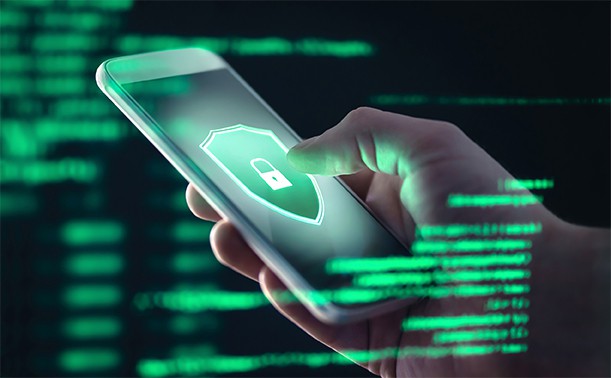 An image featuring a person holding his phone that has an antivirus logo on it and behind it green code representing mobile verification toolkit concept