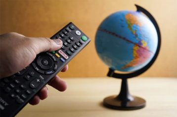 An image featuring a person holding a TV remote that has Netflix button and a globe representing Netflix VPN streaming concept