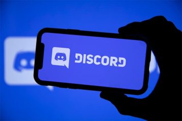An image featuring a person holding a mobile phone that has the Discord text and logo on it