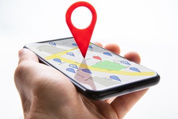 an image with persons hand holding smartphone opened on maps with red pin on it 
