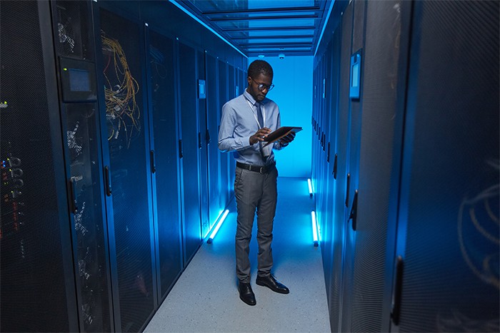 an image with a person standing in front of server cabinet and writing notes